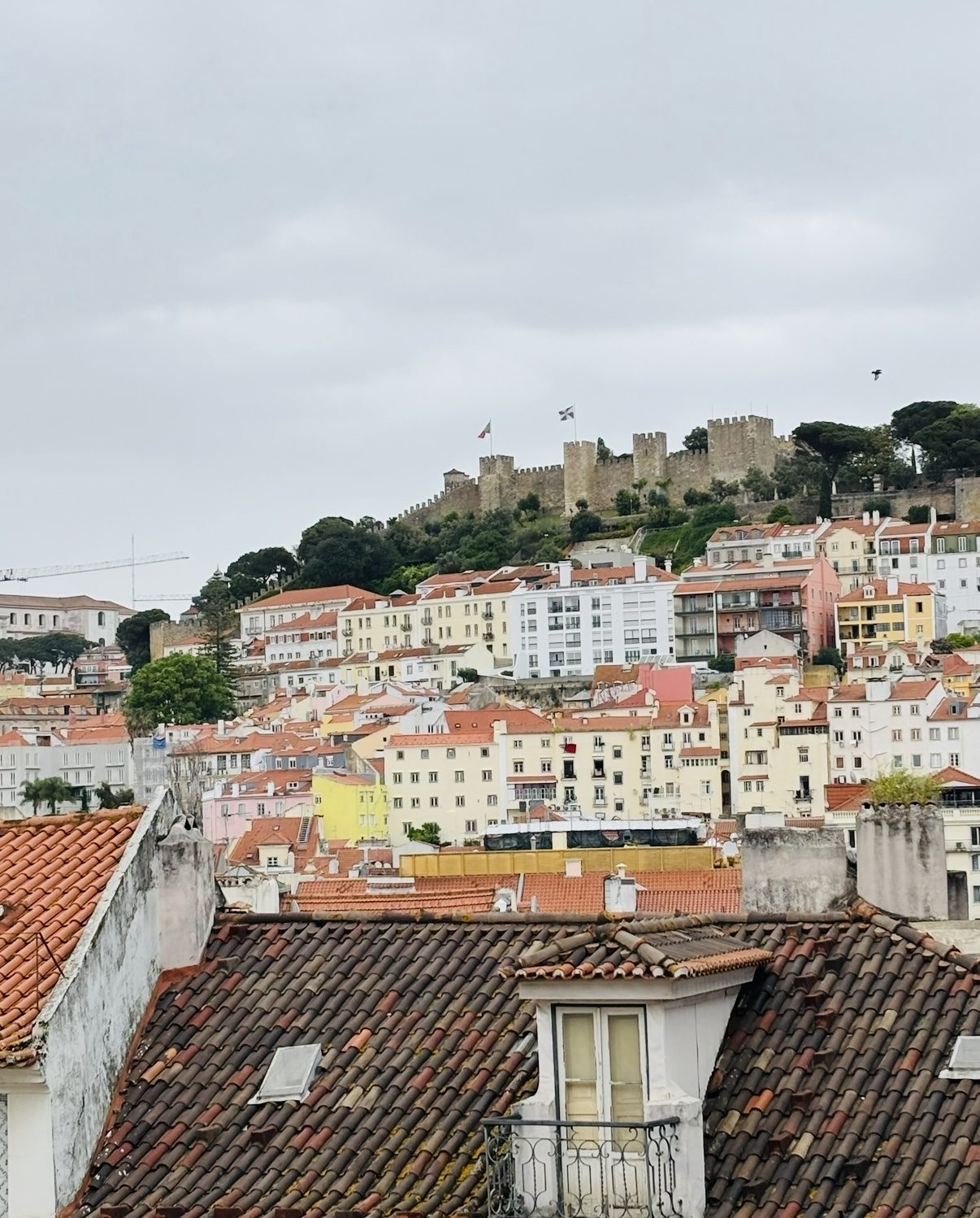 Terracotta rooftops climbing a hillside toward an old castle wall