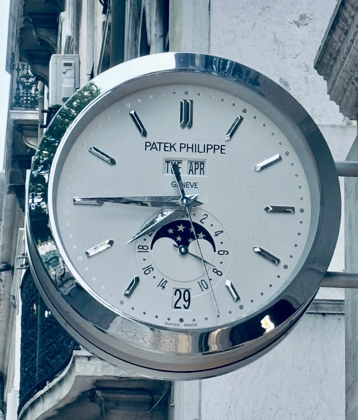 Polished street clock mounted on a weathered building facade